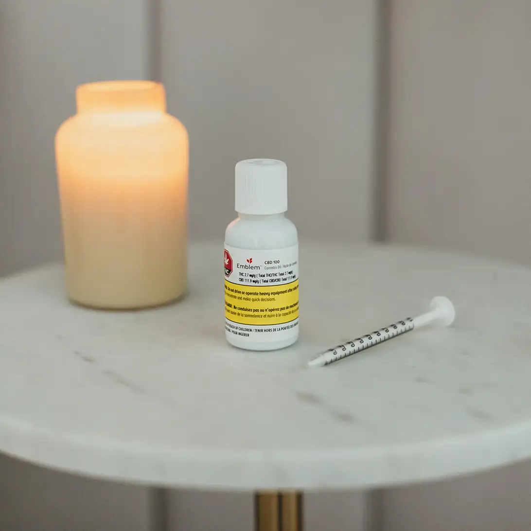 Emblem Cannabis CBD oil on a nightstand with a candle to the left and a dropper to the right